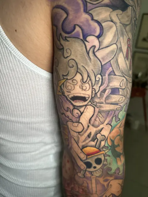 Anime arm tattoo of a white-haired figure laughing among purple clouds over a pirate flag