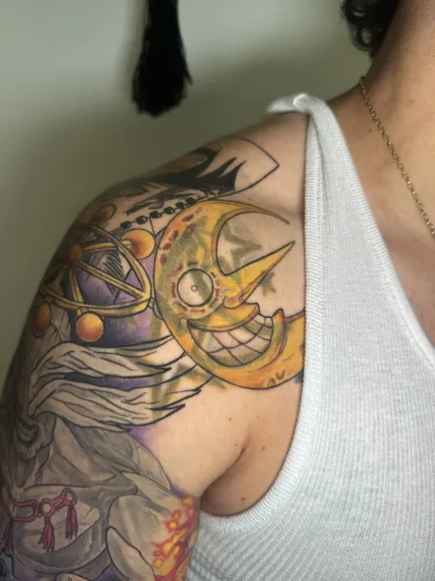 Anime shoulder view centred on the golden crescent and the ringed device across the deltoid