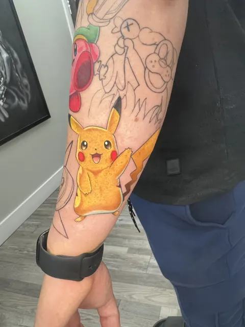 Anime forearm tattoo of Pikachu with raised arms, rendered as a die-cut sticker inside a sleeve still in linework