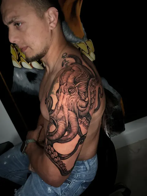 Black and grey tattoo of an octopus reaching its tentacles down the arm