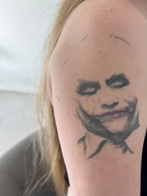 Retrato del Joker desvanecido en la parte superior del brazo, antes del cover up