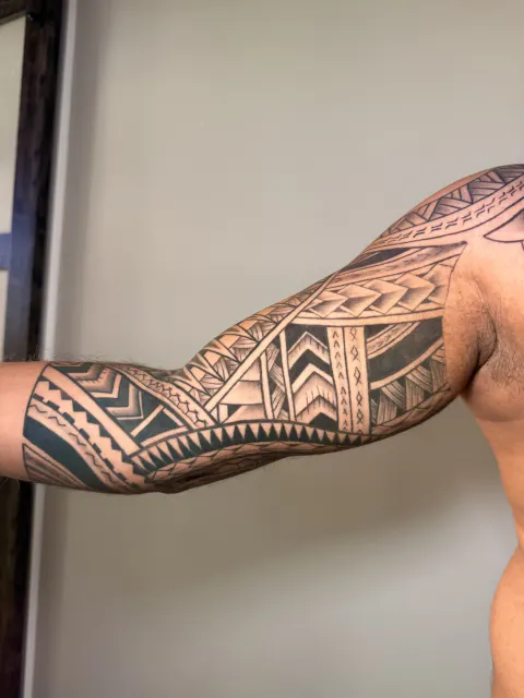Healed Polynesian blackwork sleeve running from the shoulder to the forearm