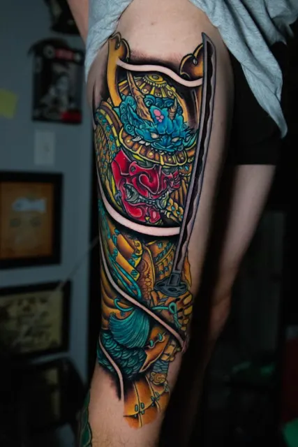 Neo-Oriental forearm tattoo of a blue samurai mask over gold armor plates