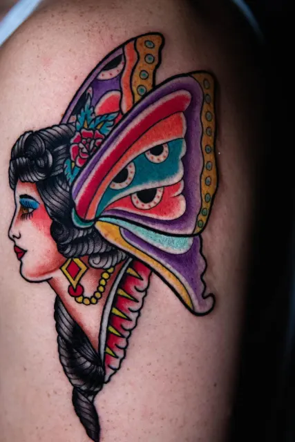 Traditional thigh tattoo of a geisha profile framed by a butterfly wing in purple, red and yellow