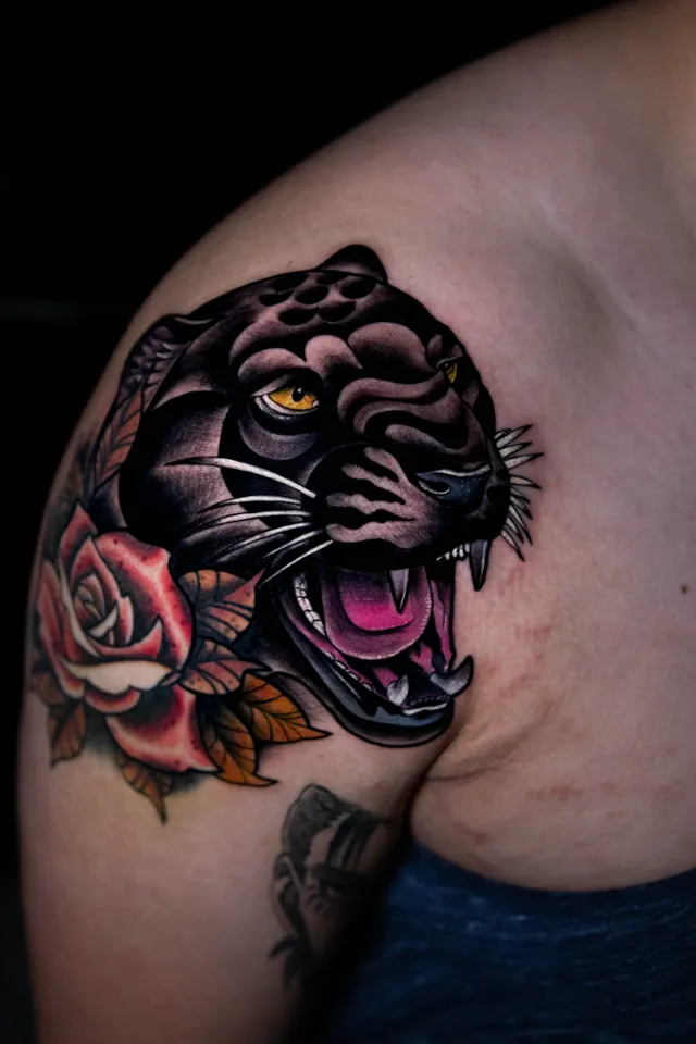 Traditional black panther tattoo framed by a red rose and green leaves